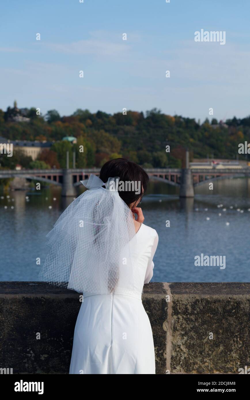 La mariée admire Prague depuis le pont Charles. Fille dans une robe de mariage avec un voile. Banque D'Images