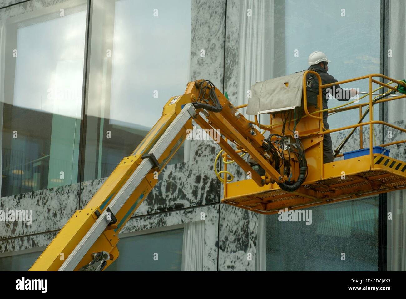 Homme lavant les fenêtres et la façade d'un bâtiment avec une vadrouille, il est debout sur une plate-forme de travail aérienne. Il porte une ceinture de sécurité et un casque. Banque D'Images