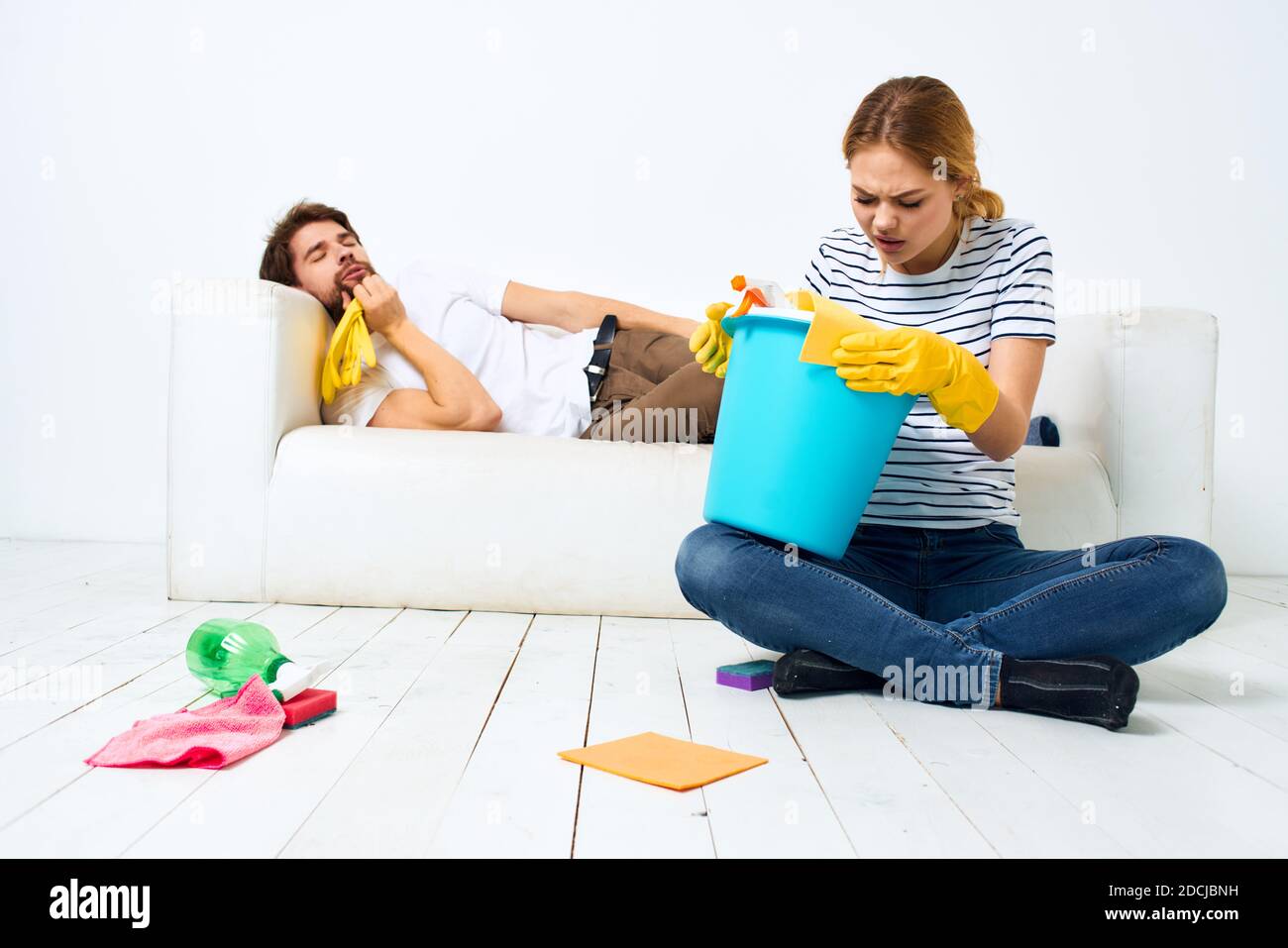 Le mari repose sur le canapé pendant que sa femme nettoie vers le haut de la décoration intérieure Banque D'Images