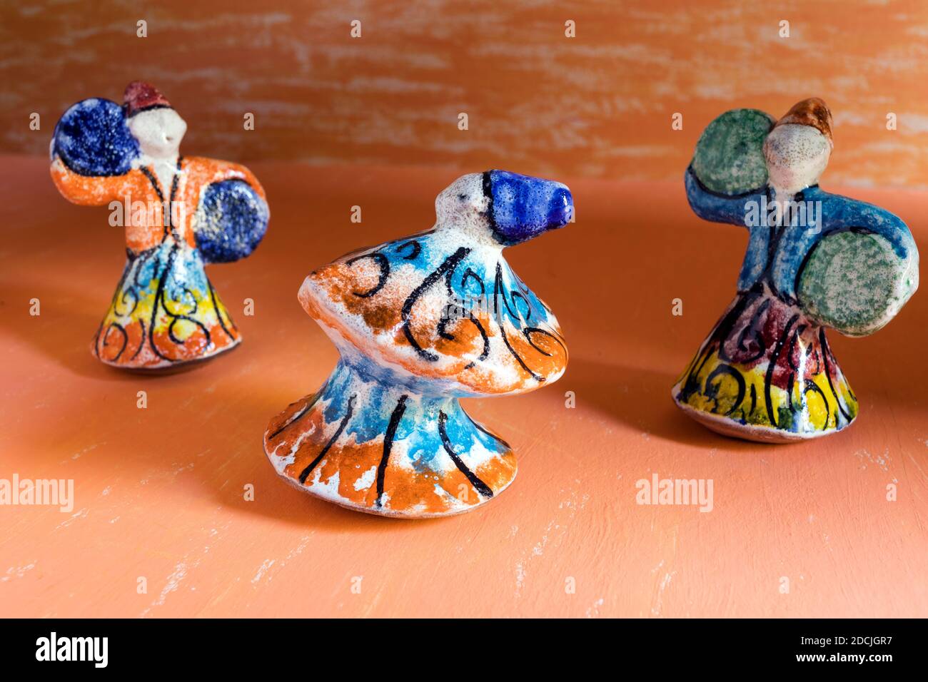 Statues en poterie de dansing Sufis avec costumes multicolores sur fond d'aquarelle orange. Banque D'Images
