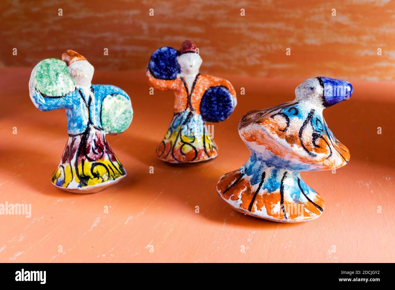 Statues en poterie de dansing Sufis avec costumes multicolores sur fond d'aquarelle orange. Banque D'Images