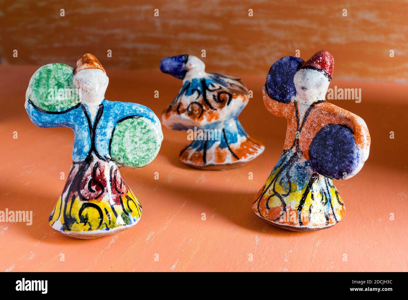 Statues en poterie de dansing Sufis avec costumes multicolores sur fond d'aquarelle orange. Banque D'Images