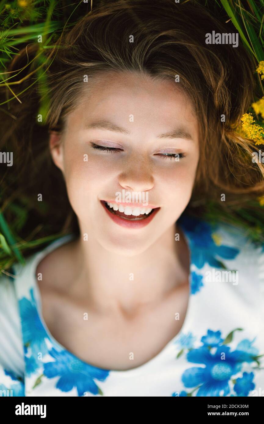 Belle mignonne souriante jeune femme caucasienne posant souriant sur l'herbe dans le champ d'été de fleurs dans une robe multicolore, vie saine Banque D'Images