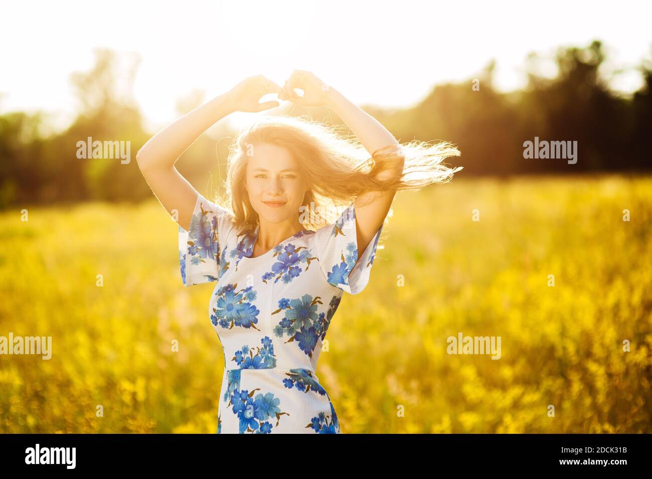 Belle tendre mignonne fille sur le champ de fleurs belle blonde femme dans le champ de fleurs dans une robe multicolore sur la lumière du coucher du soleil, vie saine Banque D'Images