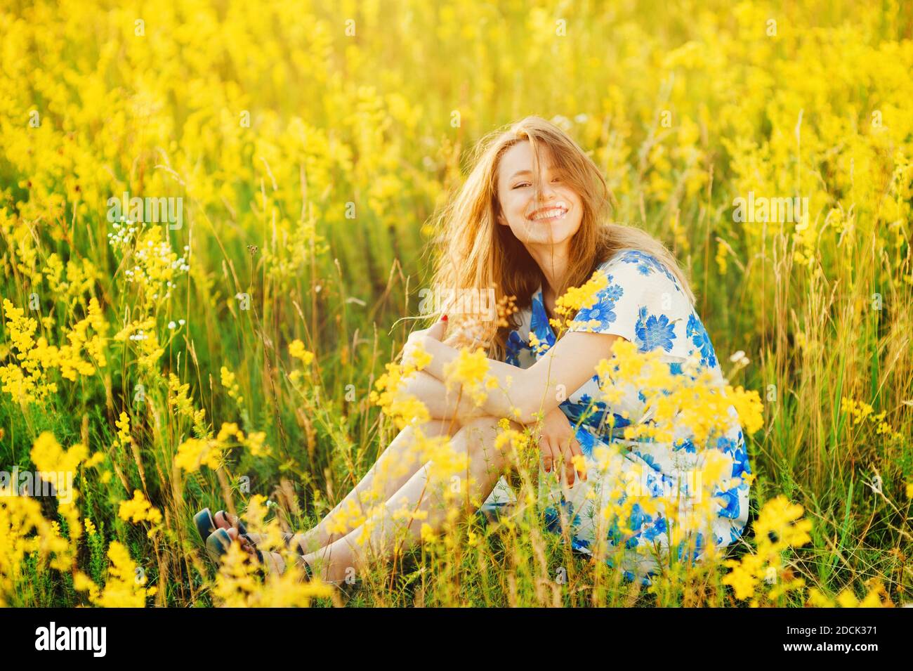 Belle fille mignonne sur le champ de fleurs belle femme blonde dans le champ de fleurs dans une robe multicolore sur la lumière du coucher du soleil, vie saine Banque D'Images