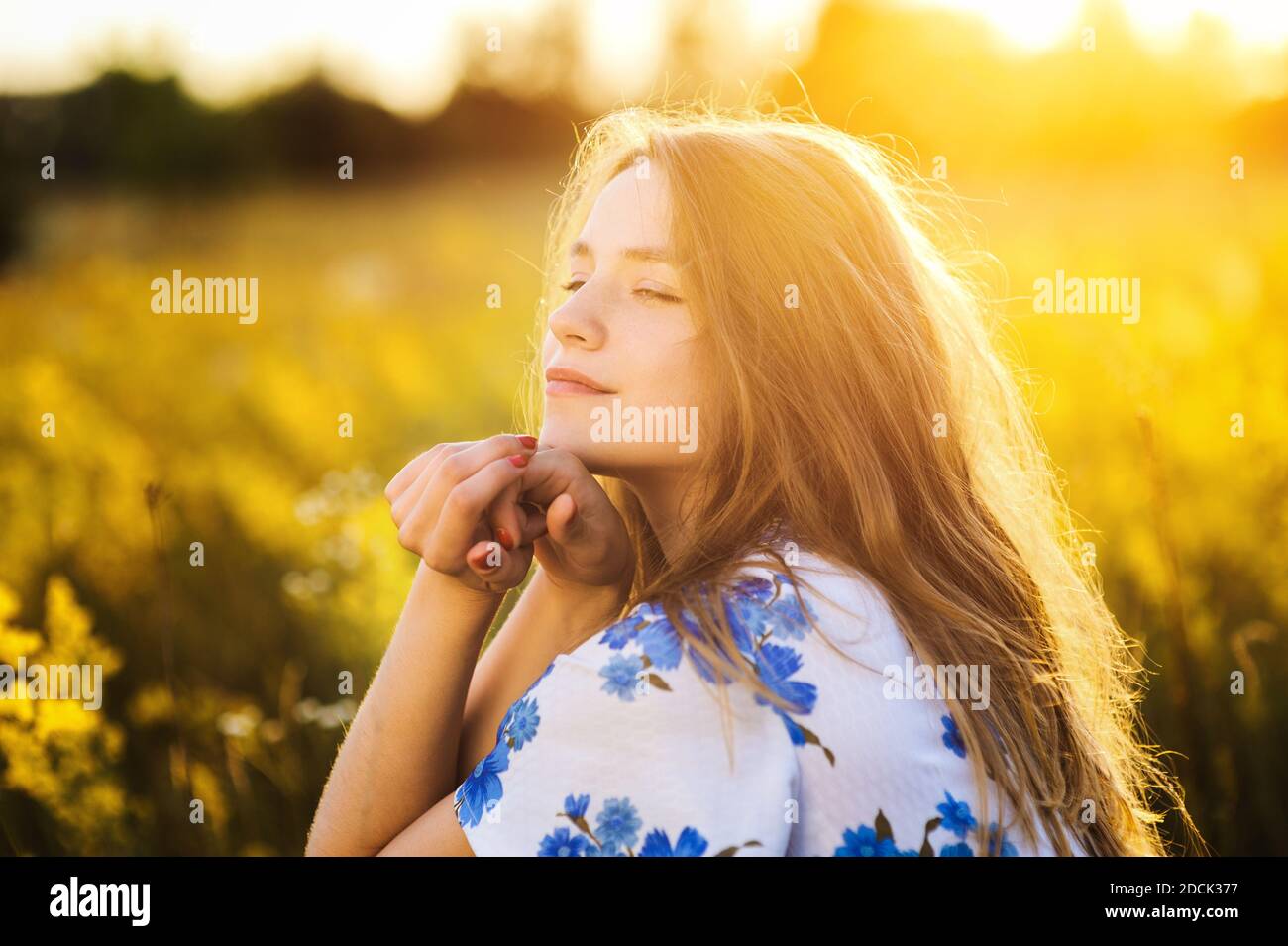 Belle fille mignonne sur le champ de fleurs belle femme blonde dans le champ de fleurs dans une robe multicolore sur la lumière du coucher du soleil, vie saine Banque D'Images