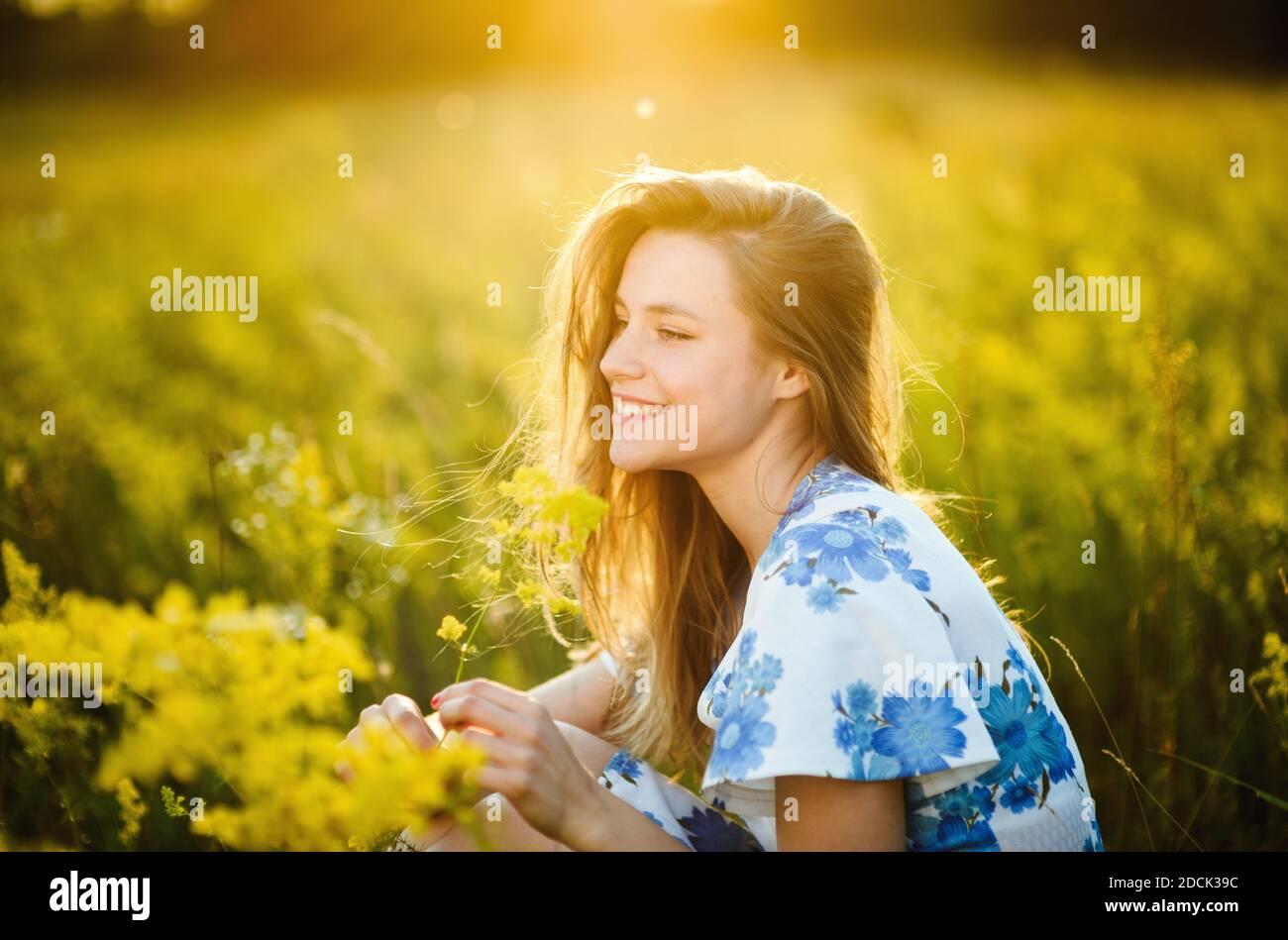 Belle tendre mignonne fille sur le champ de fleurs belle blonde femme dans le champ de fleurs dans une robe multicolore sur la lumière du coucher du soleil, vie saine Banque D'Images