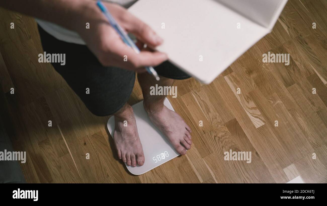 Homme marche sur des balances numériques en verre pour vérifier le poids. Poids masculin sur les pèse-personne dans les chambres domestiques, vue rapprochée des pieds. Pieds d'homme sur balance électronique Banque D'Images