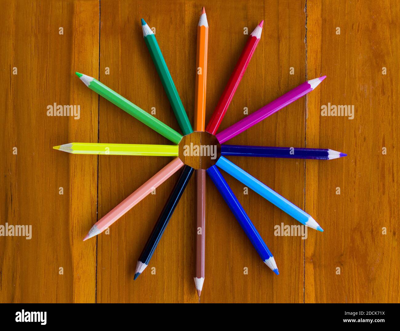 Perspective supérieure de douze crayons de couleur faisant la forme de une horloge sur fond de bois marron Banque D'Images