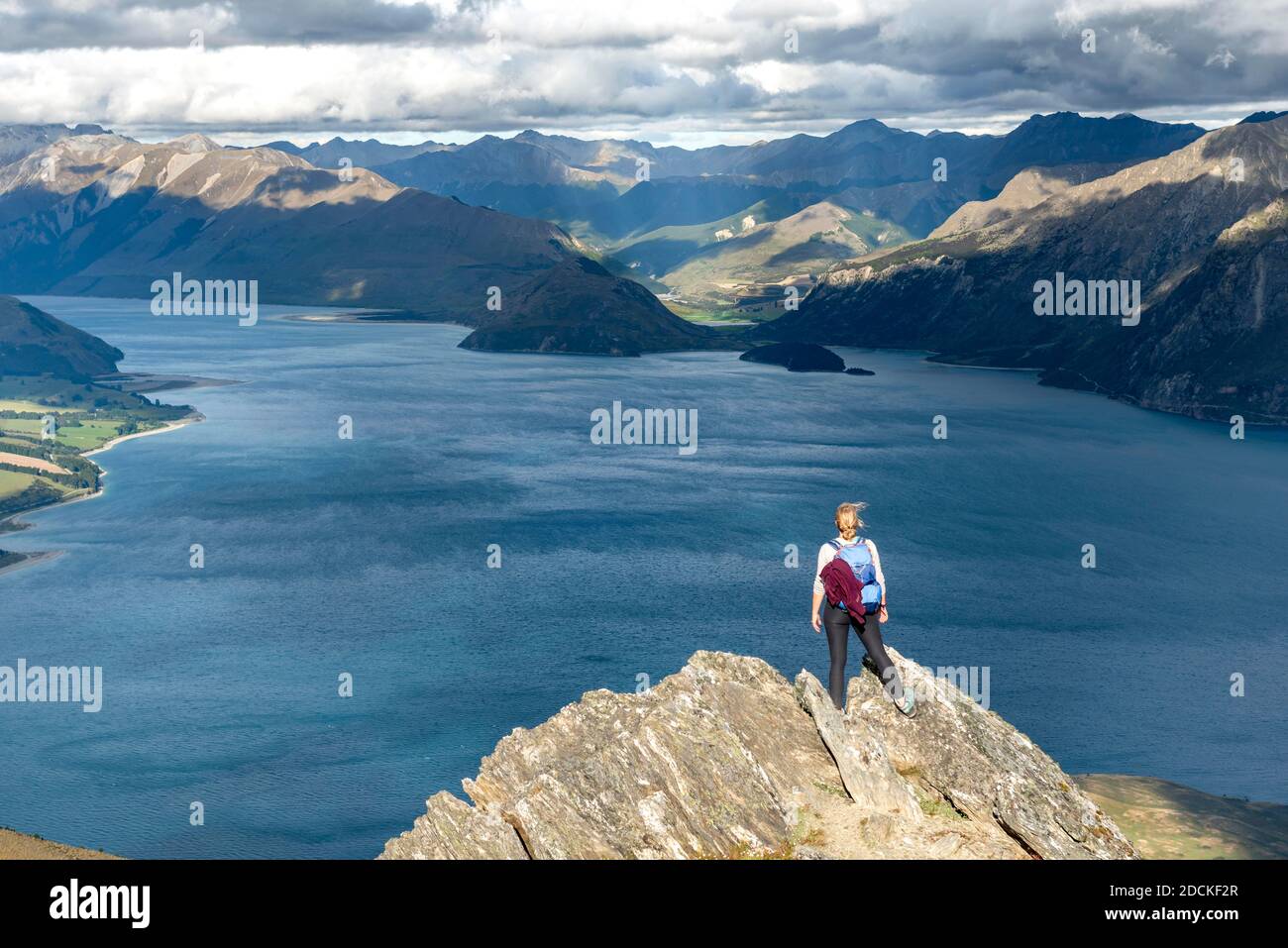 Randonneur se dresse sur un rocher, vue sur le lac Hawea, lac et paysage de montagne dans la lumière du soir, vue de Isthmus Peak, Wanaka, Otago, South Island Banque D'Images