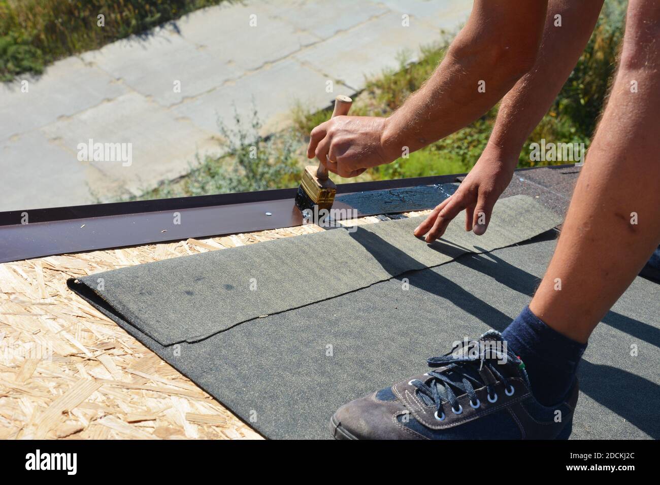 Un entrepreneur en bâtiment installe une sous-couche, une couche de ruban  de bitume sur le revêtement pour la protection globale du toit à la crête  du toit sur le Photo Stock -