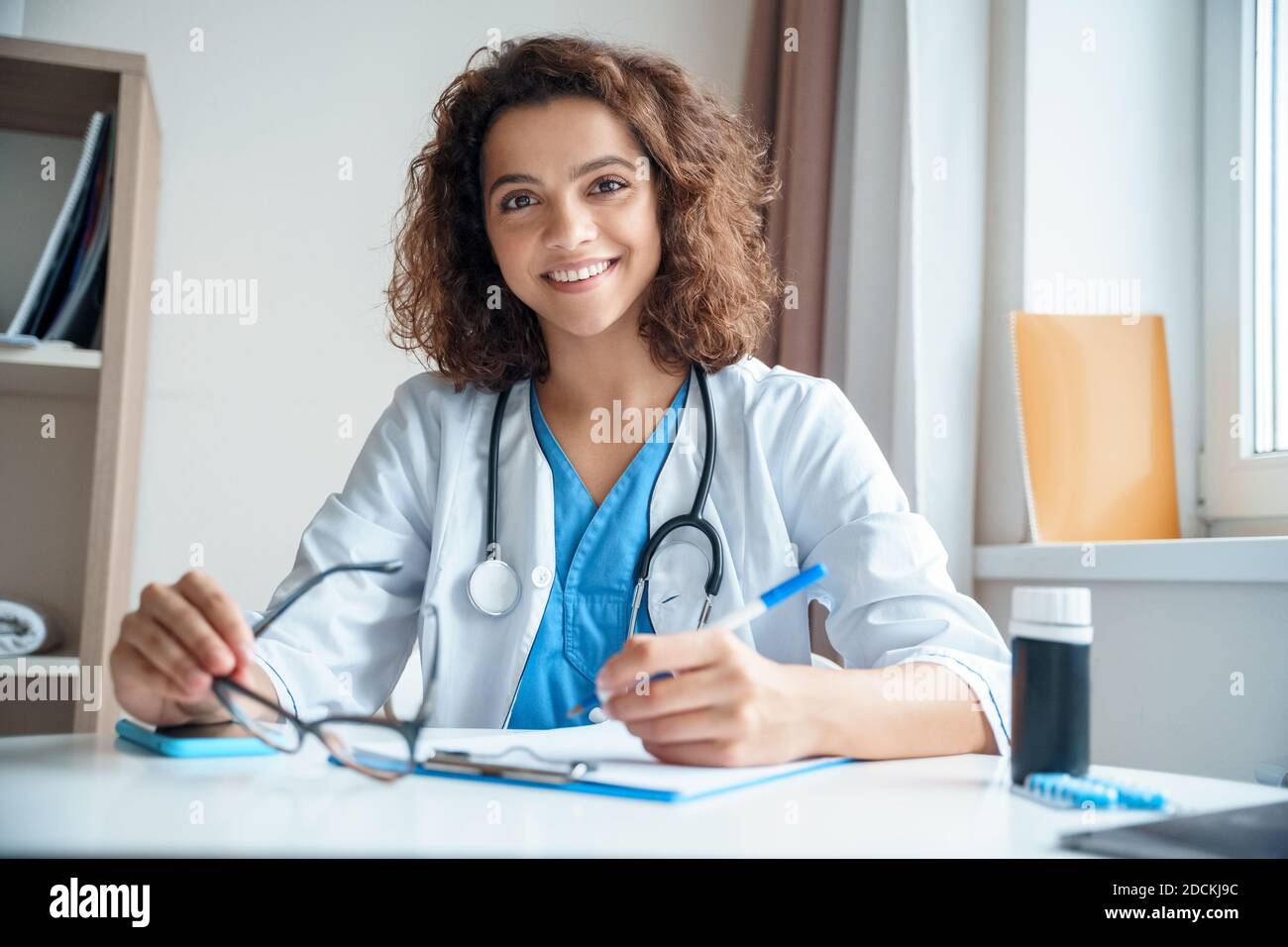 Portrait d'une femme médecin assise sur le bureau et souriant à l'appareil photo. Banque D'Images