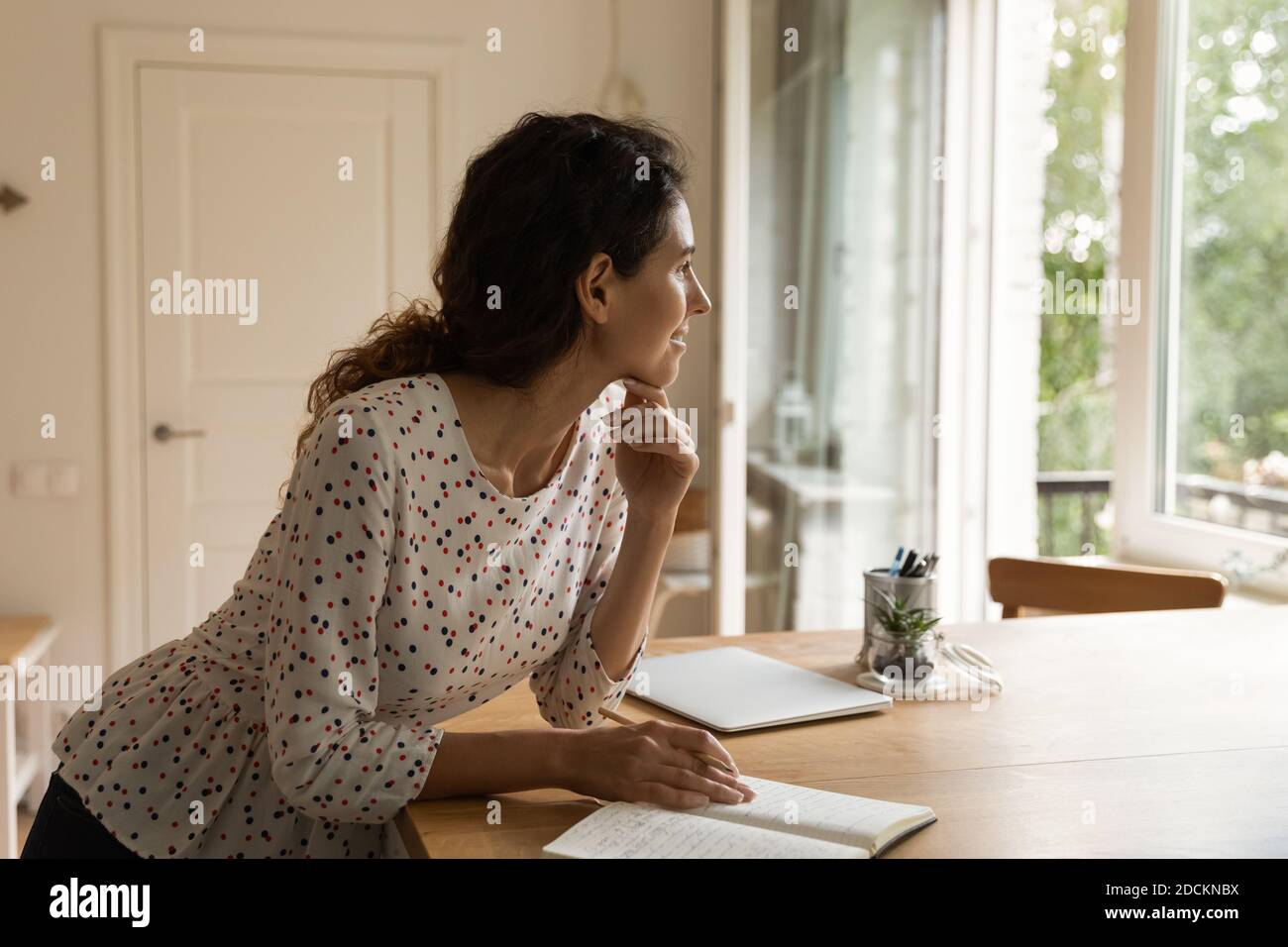 Une femme rêveuse prend des notes lors de la planification d'ordinateurs portables à la maison Banque D'Images