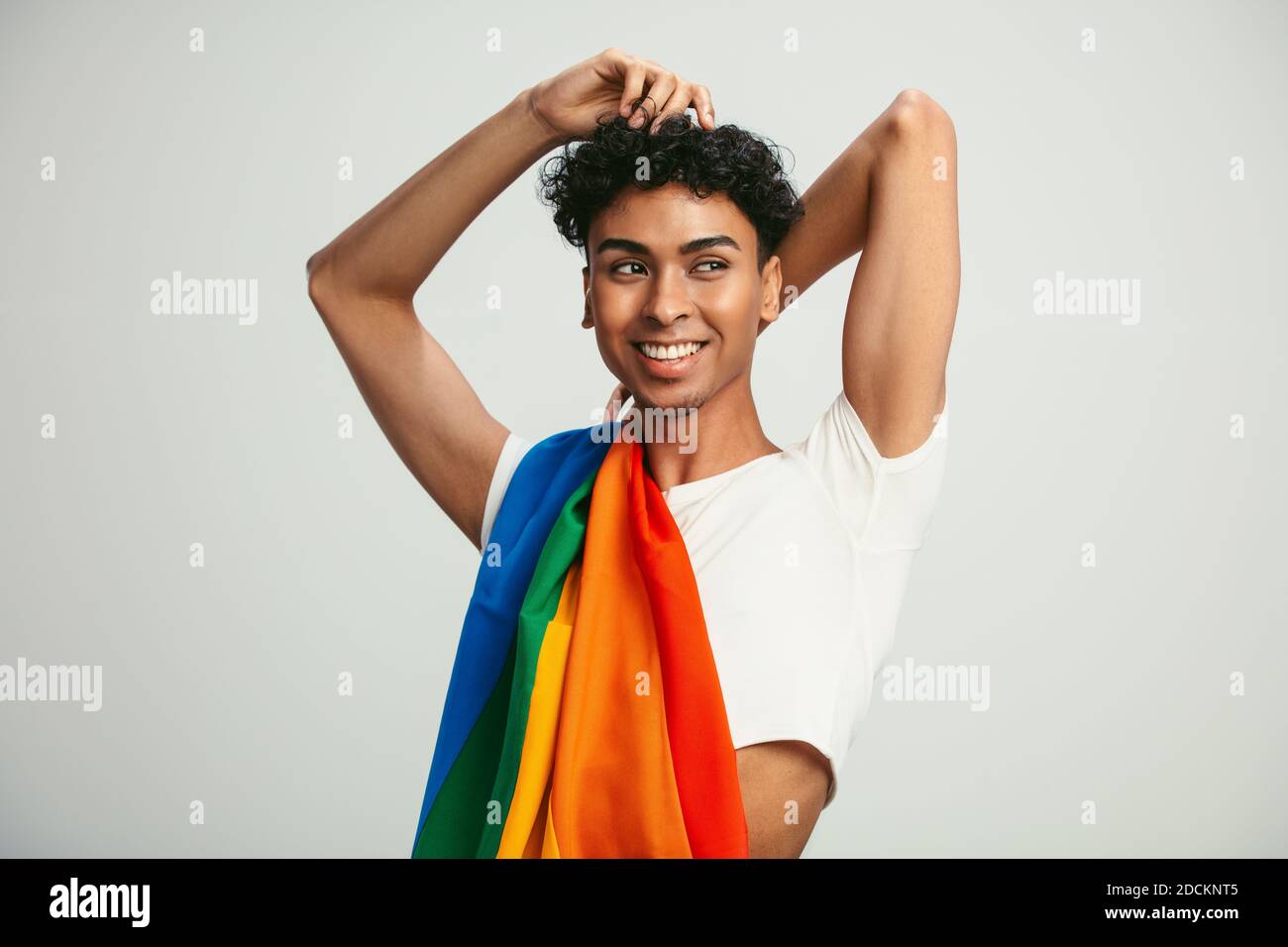 Homme avec un drapeau lgbtq sur son épaule en regardant loin. Homme gay en crop top posant sur fond blanc. Banque D'Images