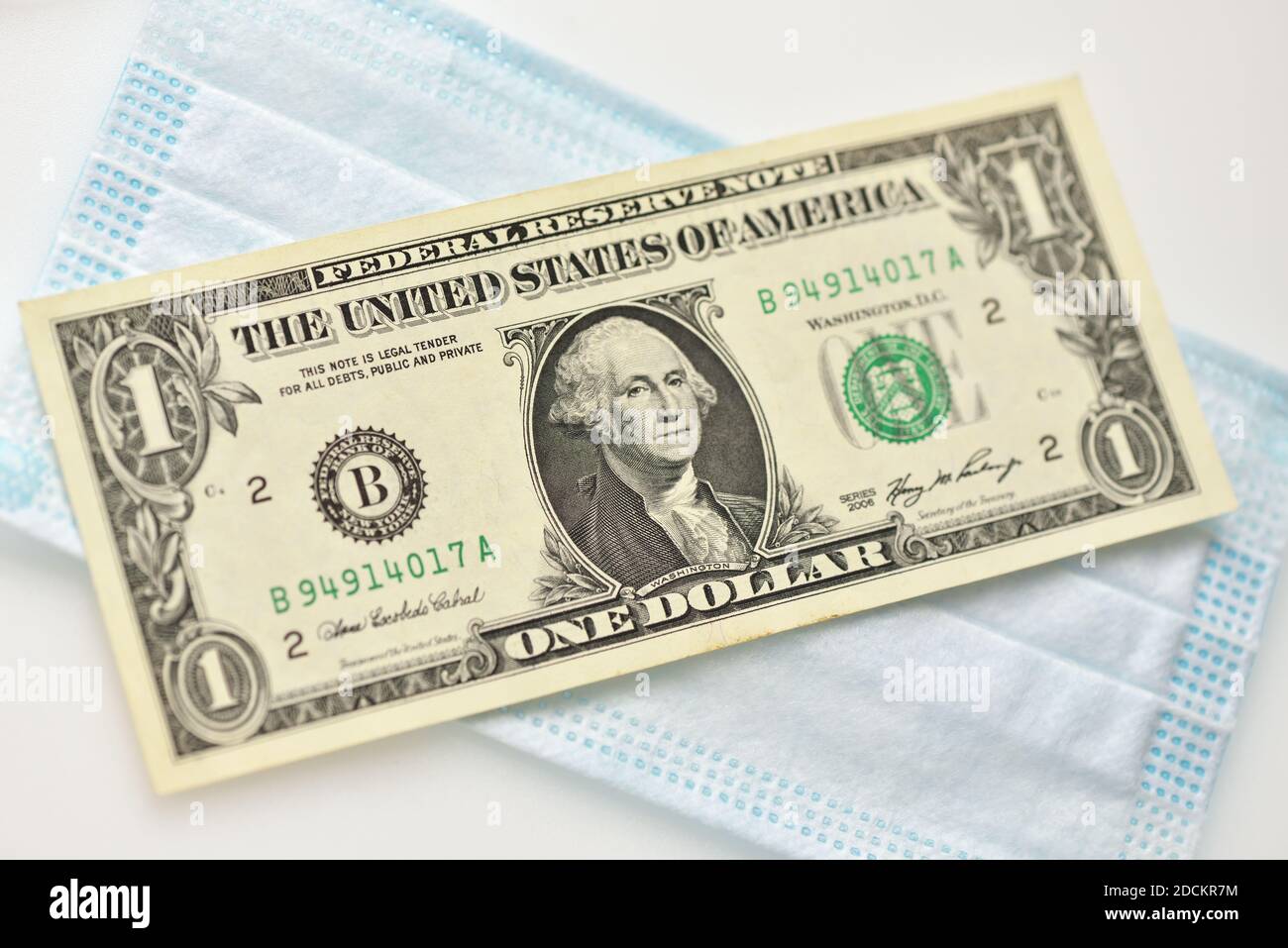 Une facture d'un dollar repose sur un masque médical sur fond blanc Banque D'Images
