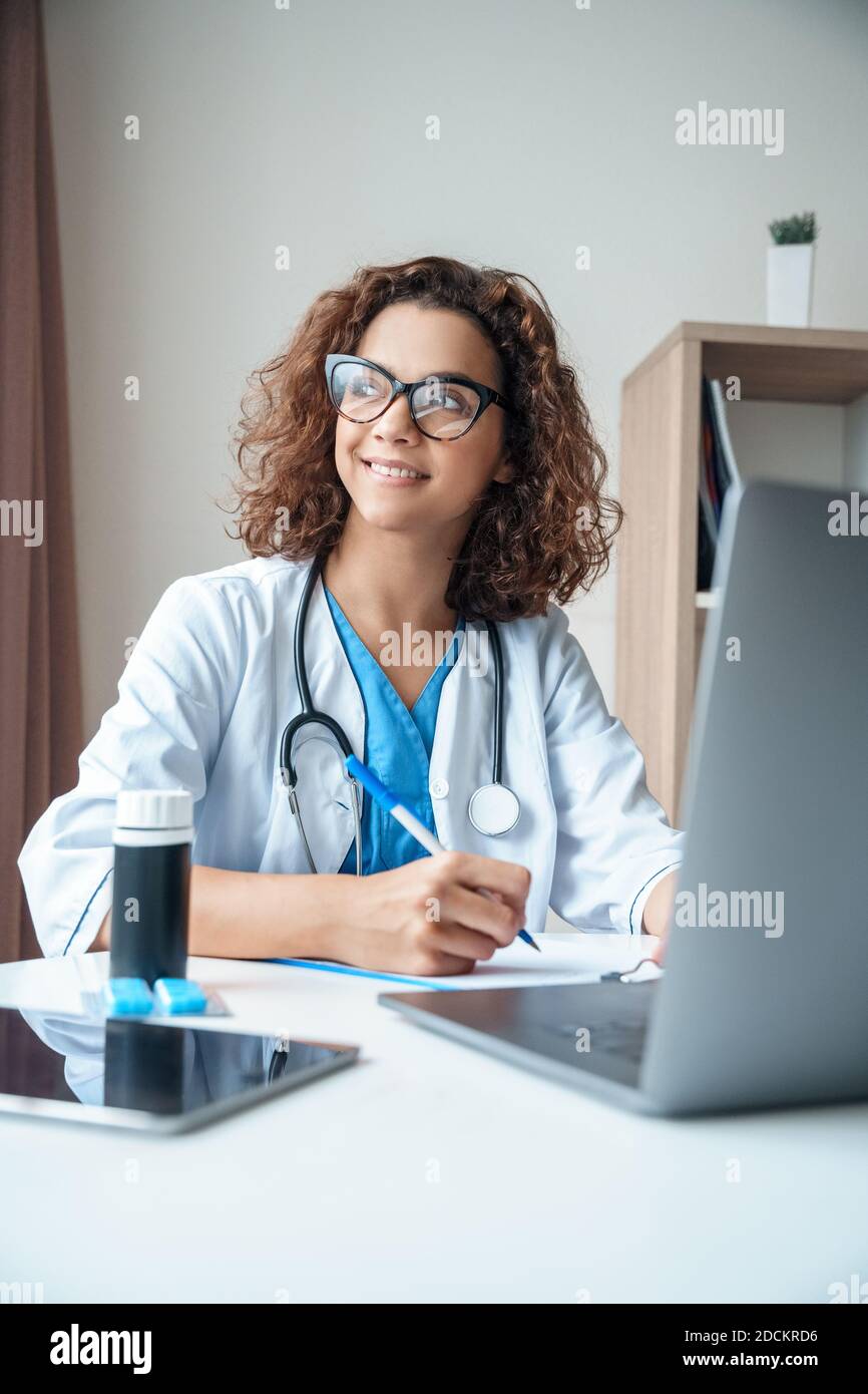 Portrait vertical d'une femme médecin assise sur le bureau et souriante. Banque D'Images