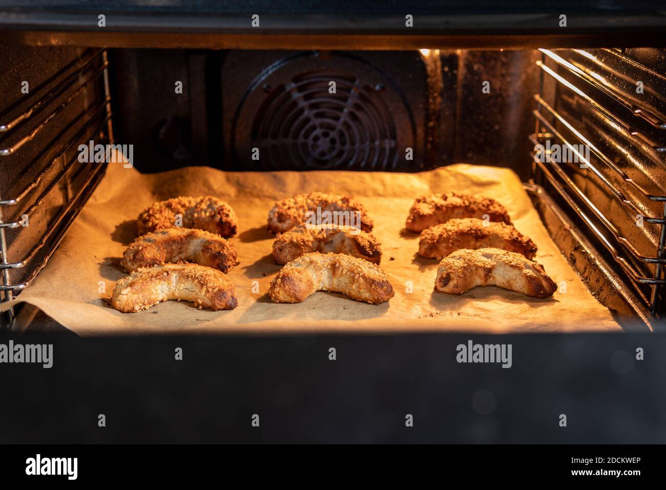 De délicieux croissants d'amande végétalienne fraîchement cuits avec des amandes hachées sur une plaque de cuisson dans un four éclairé. C'est une savoureuse pâtisserie macaron avec du massepain. Banque D'Images