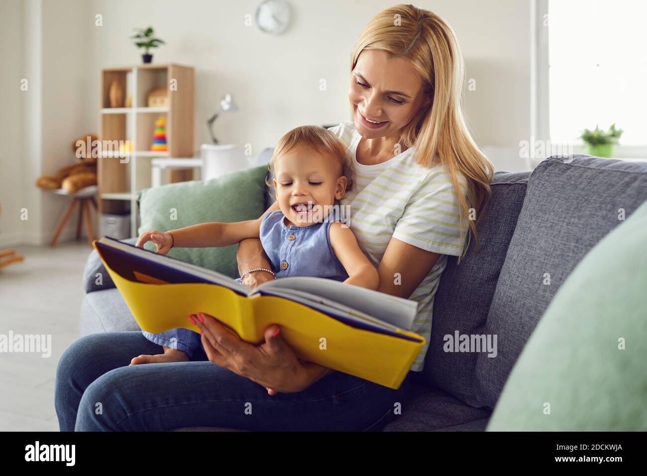 Mère heureuse avec bébé souriant sur les genoux et livre de lecture à la maison Banque D'Images