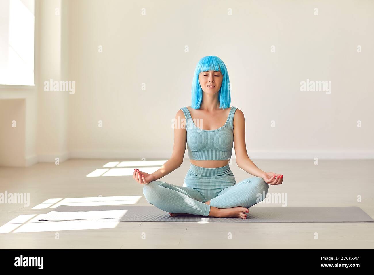 Jeune femme assise en position facile sur un tapis de yoga avec les yeux fermés en profitant d'un moment de calme seul Banque D'Images