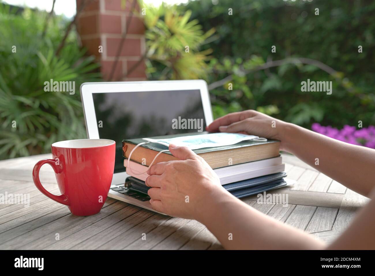 Femme mains sur des livres empilés avec masque sur le dessus de l'ordinateur portable ouvert avec une tasse rouge. Étudier à domicile pendant le concept de pandémie. Banque D'Images