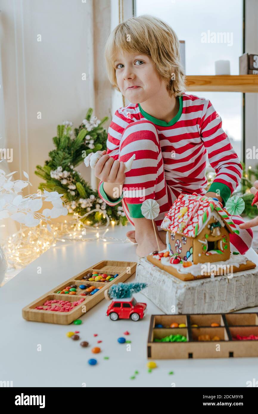 Les enfants ont décoré la maison de pain d'épice de Noël avec glaçant coloré et bonbons sur la table dans la cuisine. Noël famille maison activités concep Banque D'Images