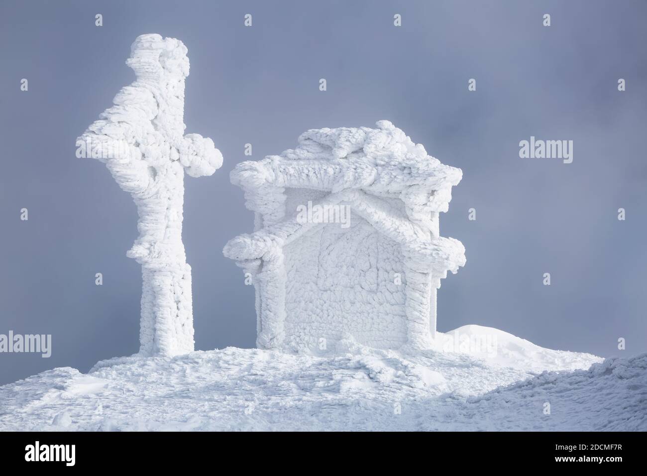 Sur la pelouse il y a une église en bois couverte de neige sur les montagnes. Brouillard sur l'arrière-plan. Paysage d'hiver fantastique. Banque D'Images