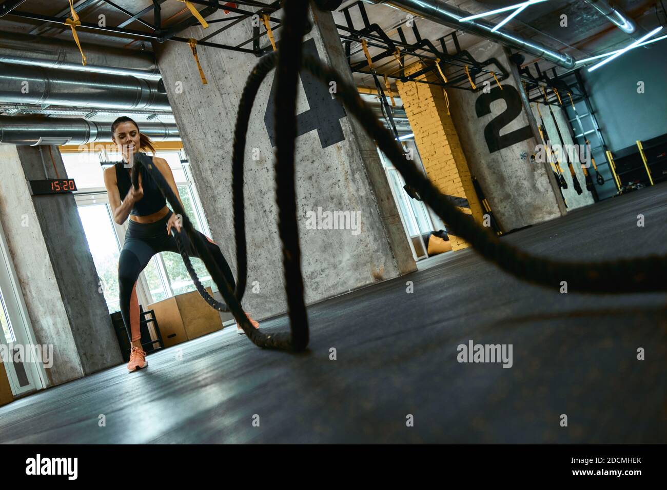 Entraînement CrossFit. Jeune femme sportive forte portant des vêtements de sport s'exerçant avec des cordes de combat à la salle de gym, pleine longueur. Sport, entraînement et mode de vie sain Banque D'Images