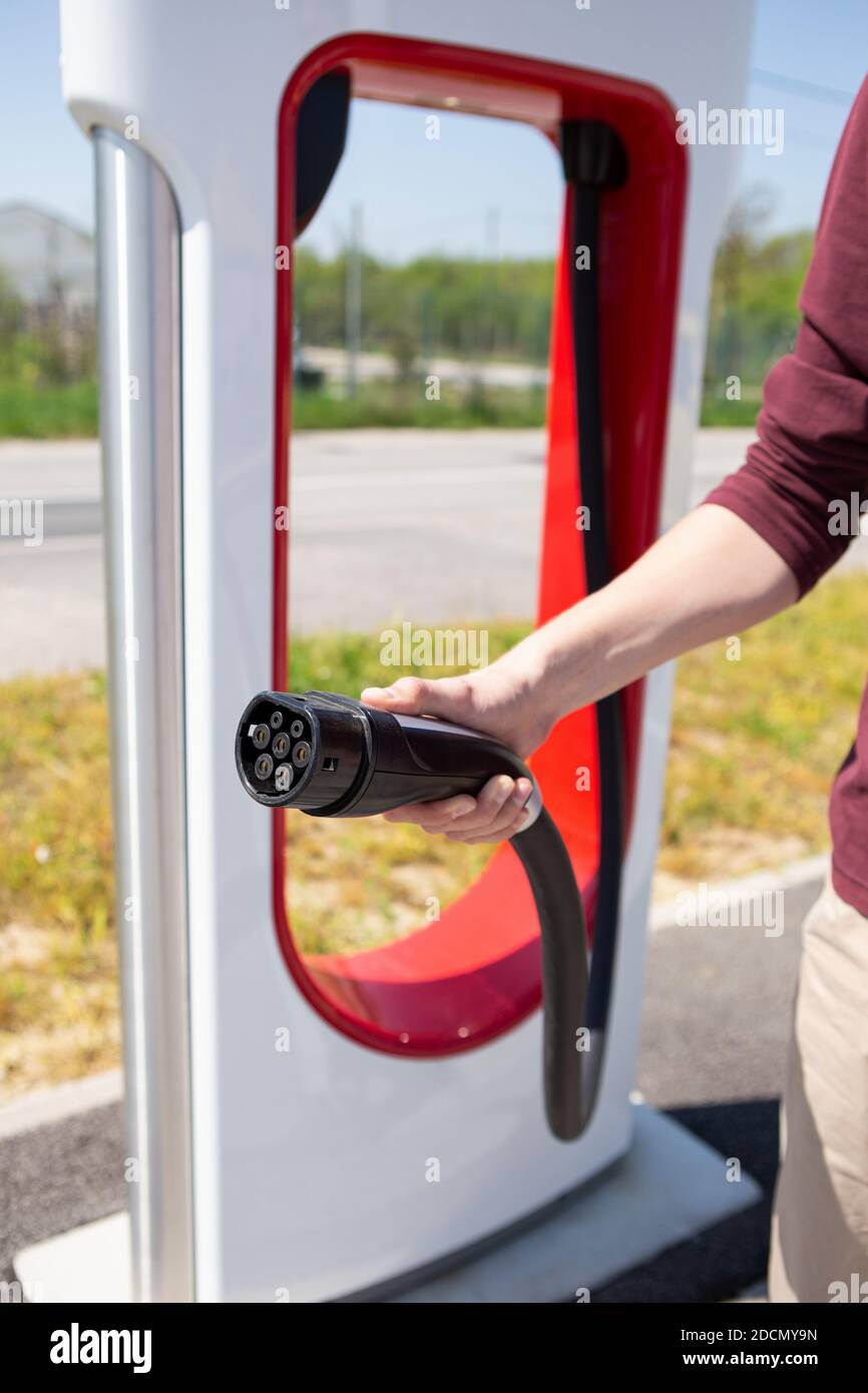 Un homme tient une fiche de chargeur pour une voiture électrique Banque D'Images