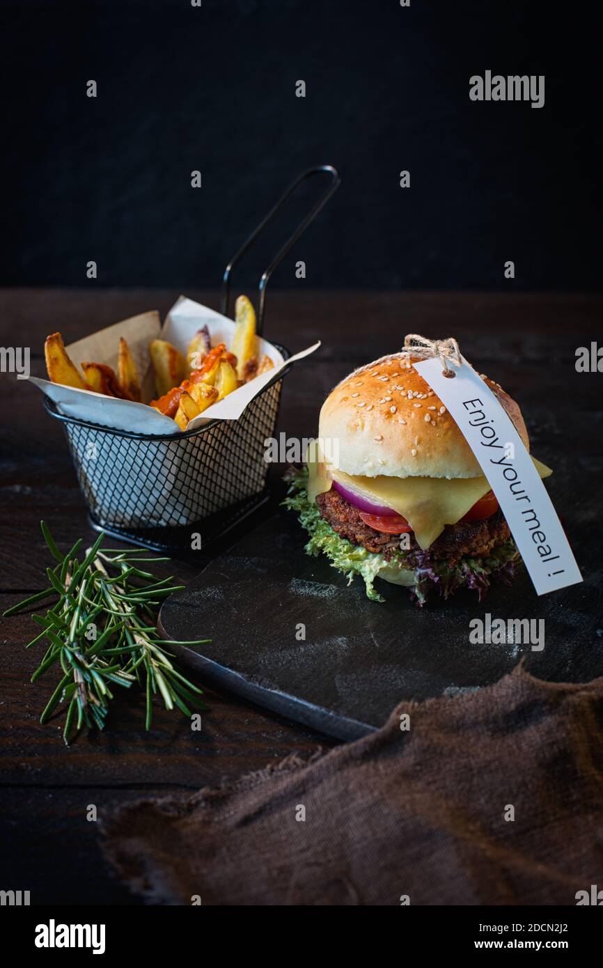 Hamburgers au fromage végétarien faits maison et frites dans une obscurité panneau en bois sur une table en bois brun foncé à côté Une serviette de table en lin brun avec un signe de plaisir Banque D'Images