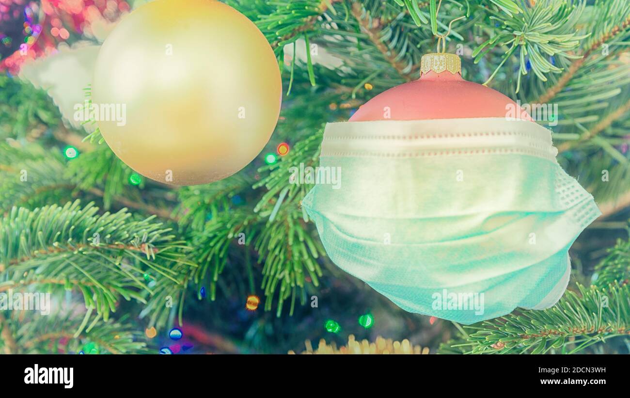 Boule de Noël portant un masque de visage. Célébrer en toute sécurité les fêtes pendant le concept de pandémie de COVID. Filtre froid. Banque D'Images