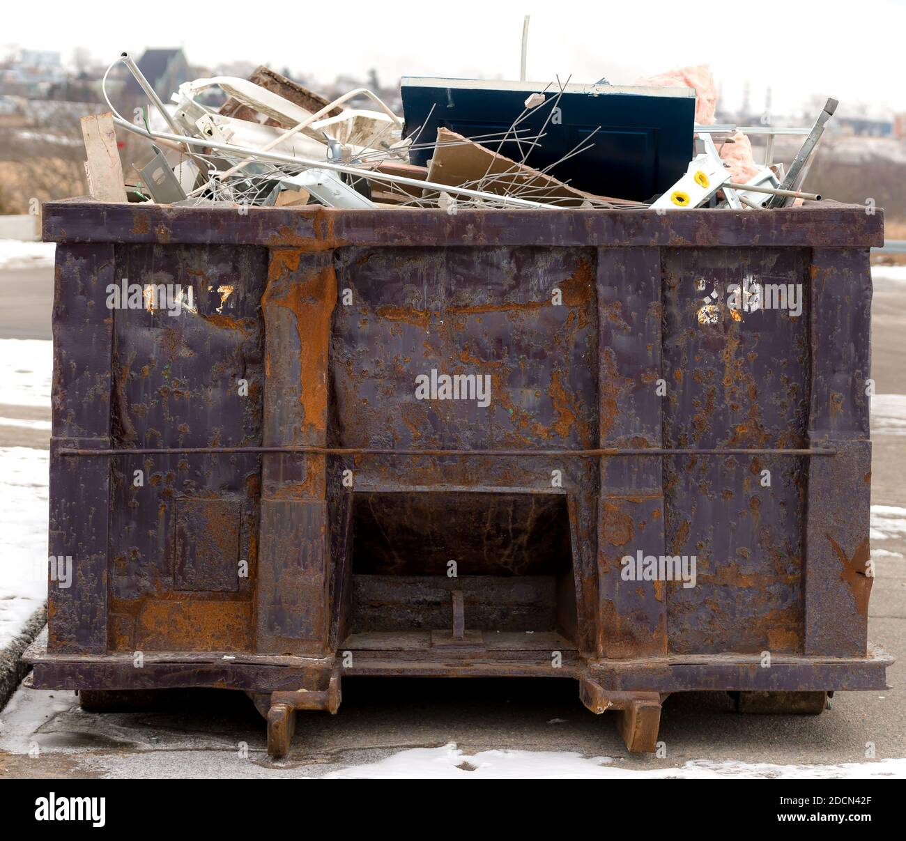 Grande poubelle en métal rouillé. Le bac est rempli de déchets et de la malbouffe, la plupart semblent être des déchets de construction. Banque D'Images