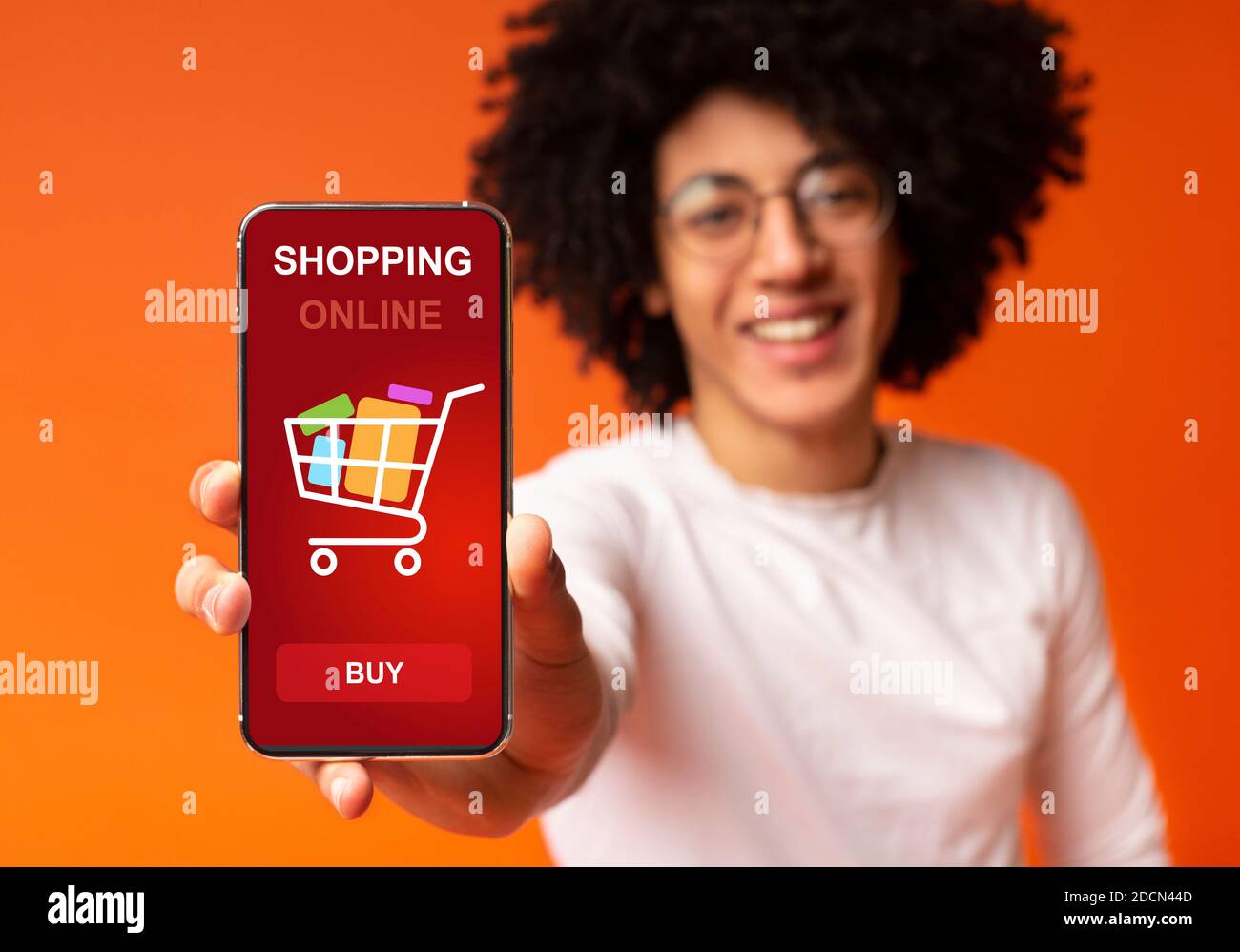 Guy faisant la démonstration d'un smartphone avec une application d'achat qui pose sur un fond Orange Banque D'Images