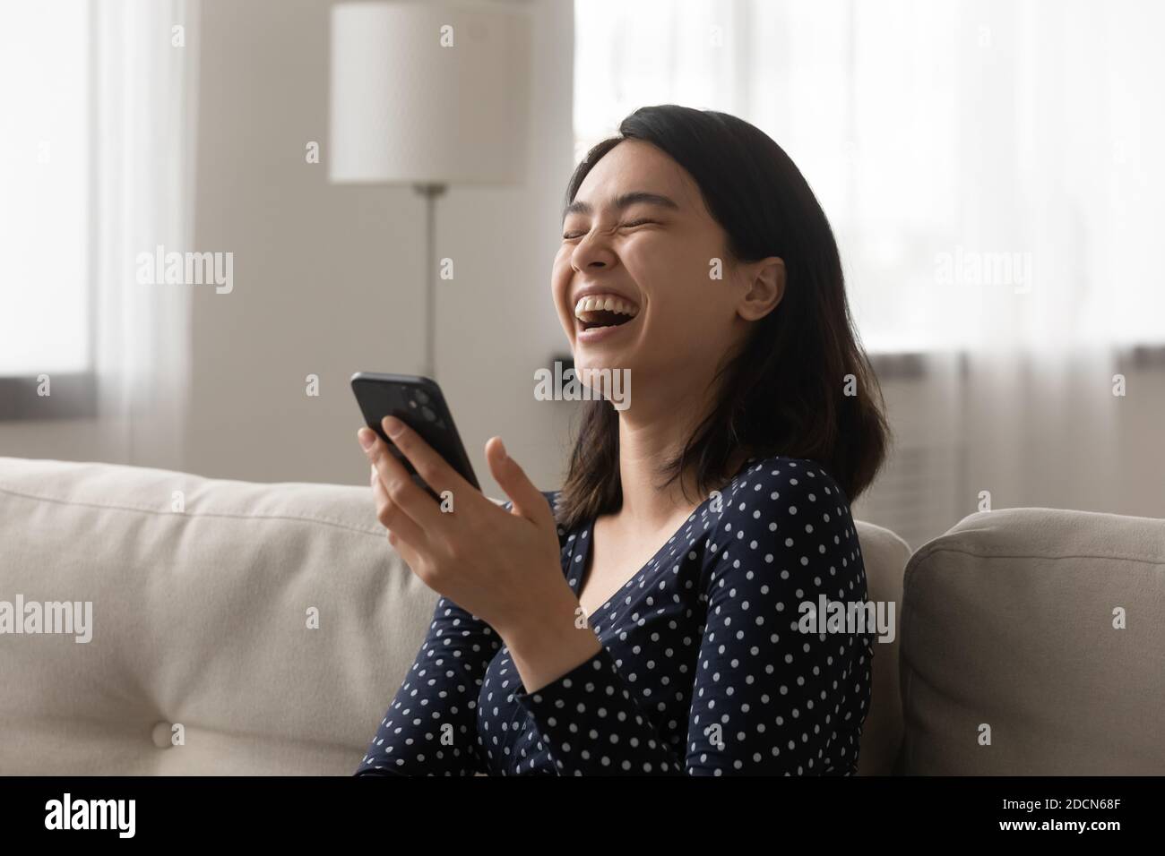 Gros plan une femme asiatique joyeuse riant à haute voix, tenant son smartphone Banque D'Images