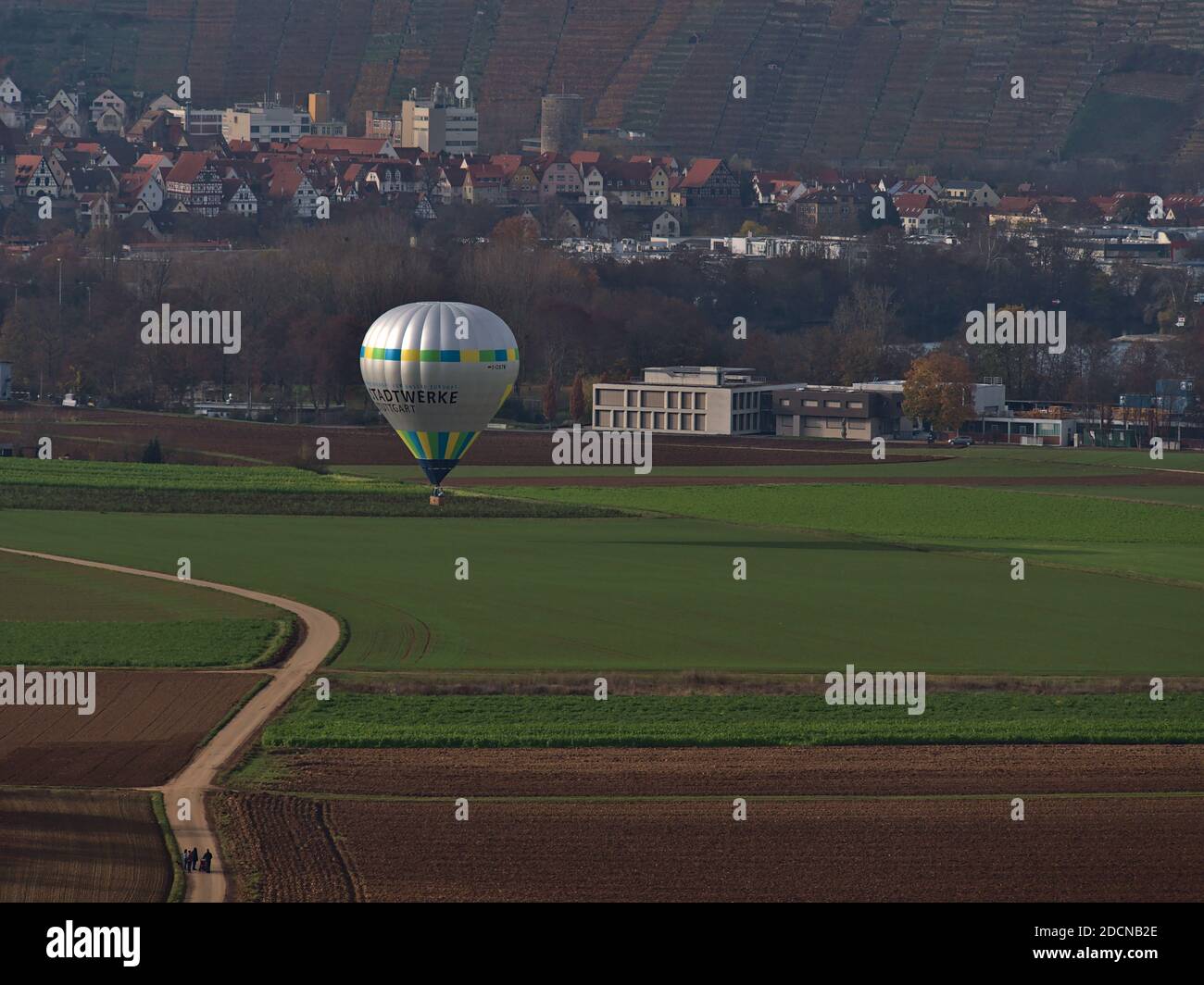 Ballon à air chaud marqué par la société de services publics Stadtwerke Stuttgart sur le point d'atterrir sur le terrain agricole en face de la ville de Besigheim avec des randonneurs . Banque D'Images