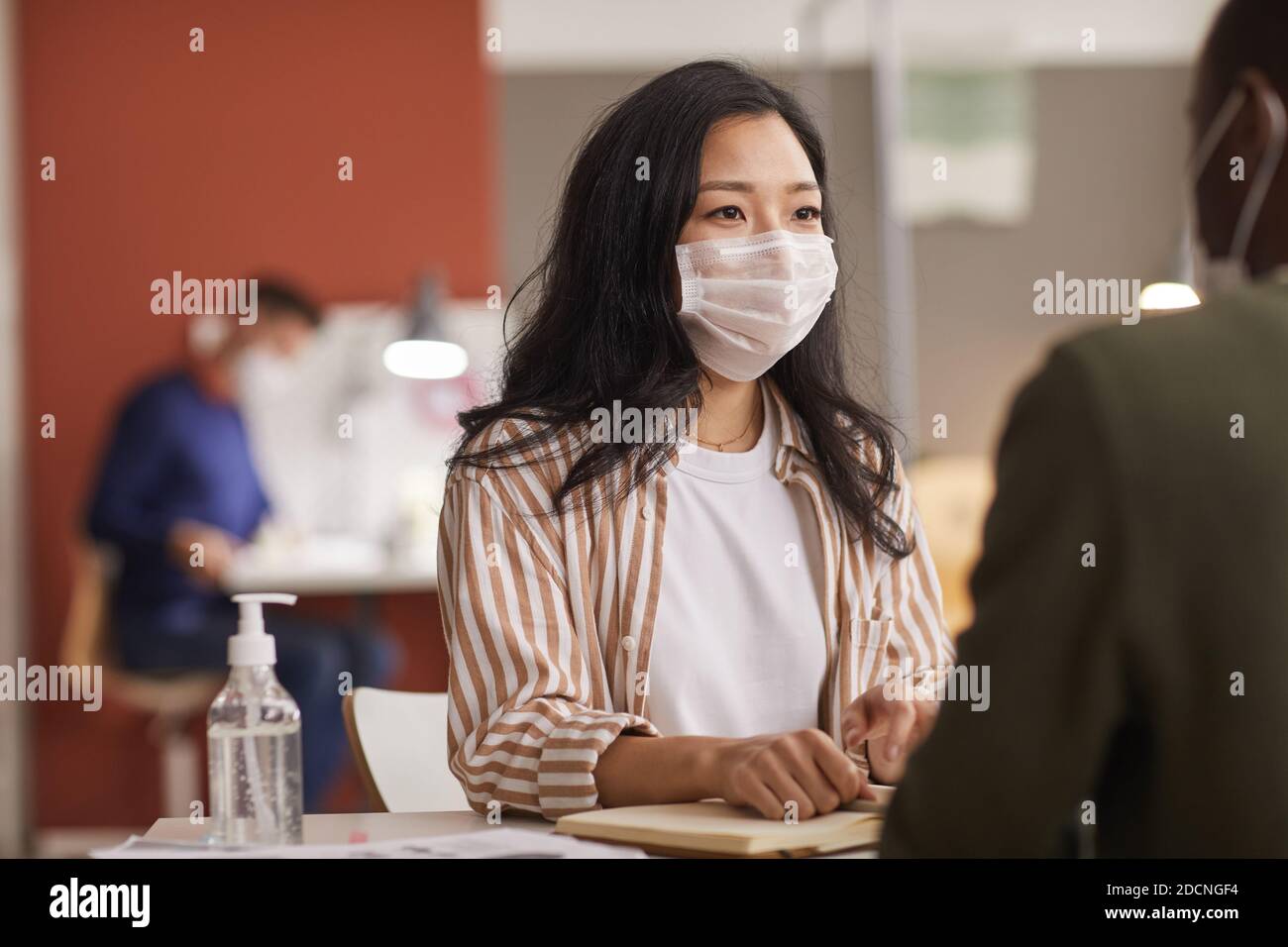 Portrait d'une jeune femme asiatique portant un masque lors d'une réunion d'affaires au bureau avec une bouteille d'assainisseur au premier plan, espace réservé aux copies Banque D'Images