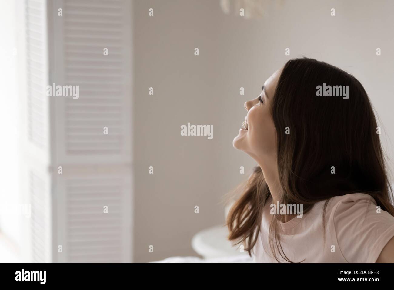 Une femme souriante se réveillant assis sur le lit donnant sur la fenêtre Banque D'Images