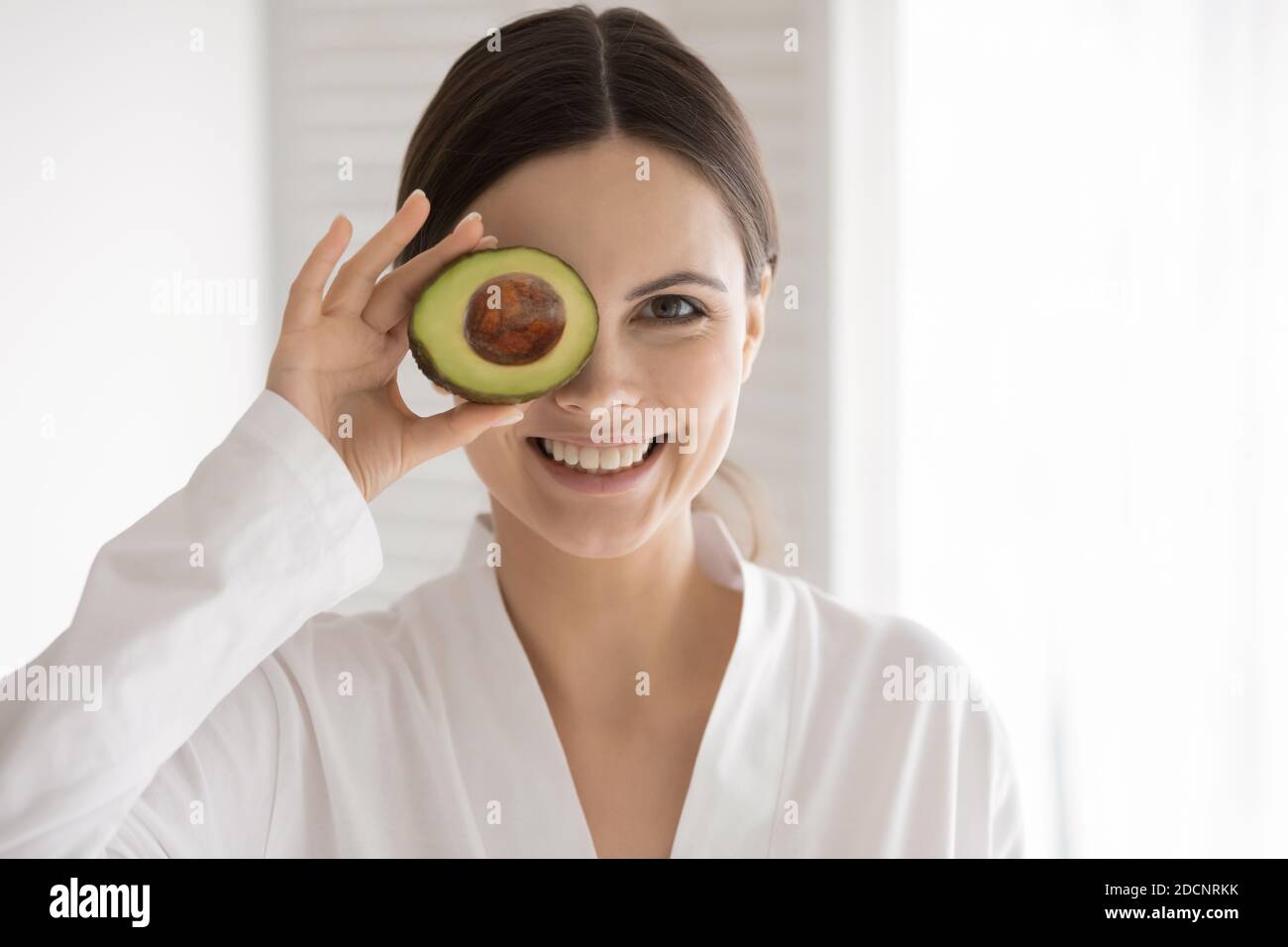 Joyeuse femme avec une peau saine qui cache l'œil derrière la tranche d'avocat Banque D'Images