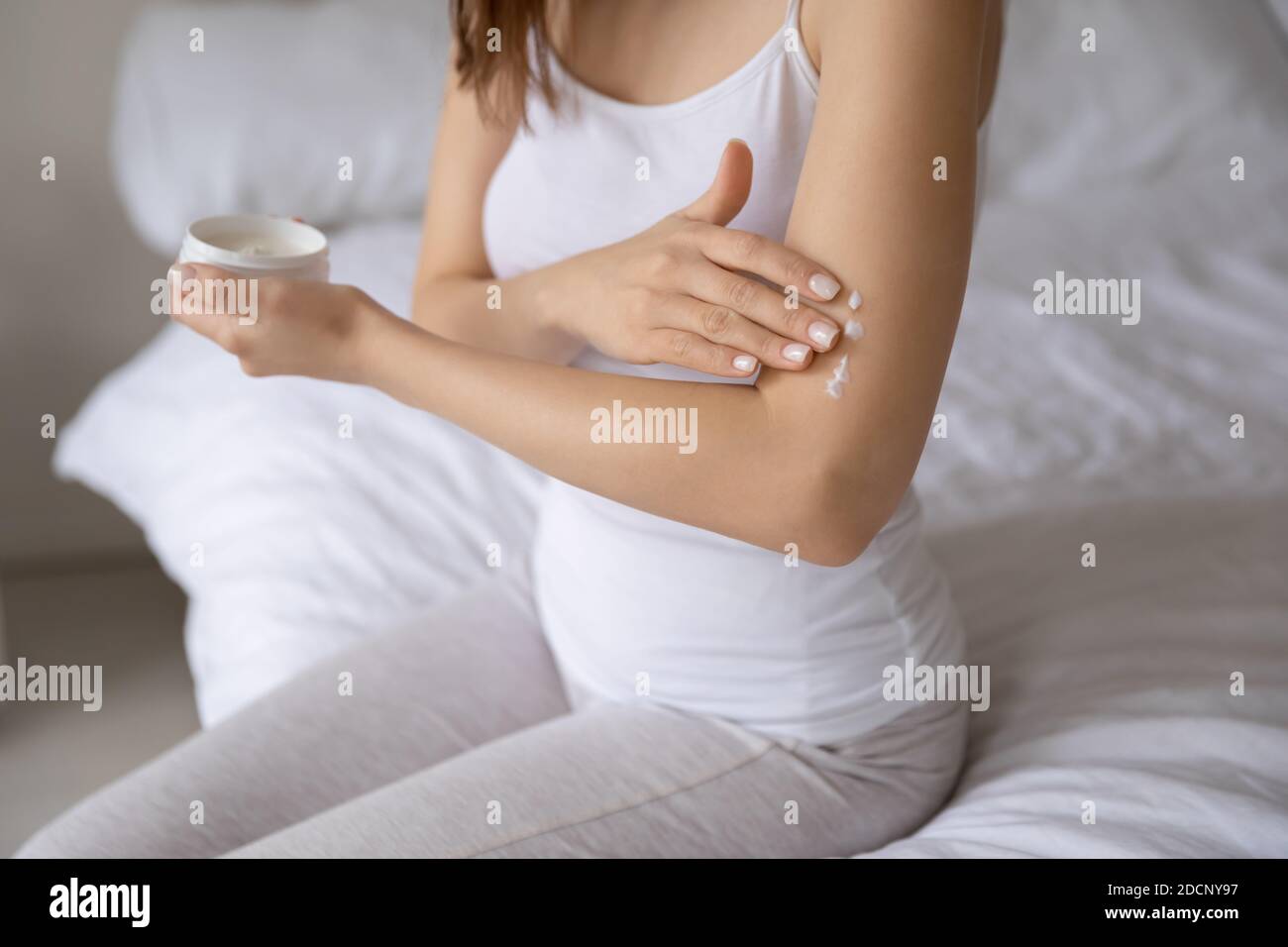 Jeune femme assise sur le lit prenant soin de sa peau Banque D'Images