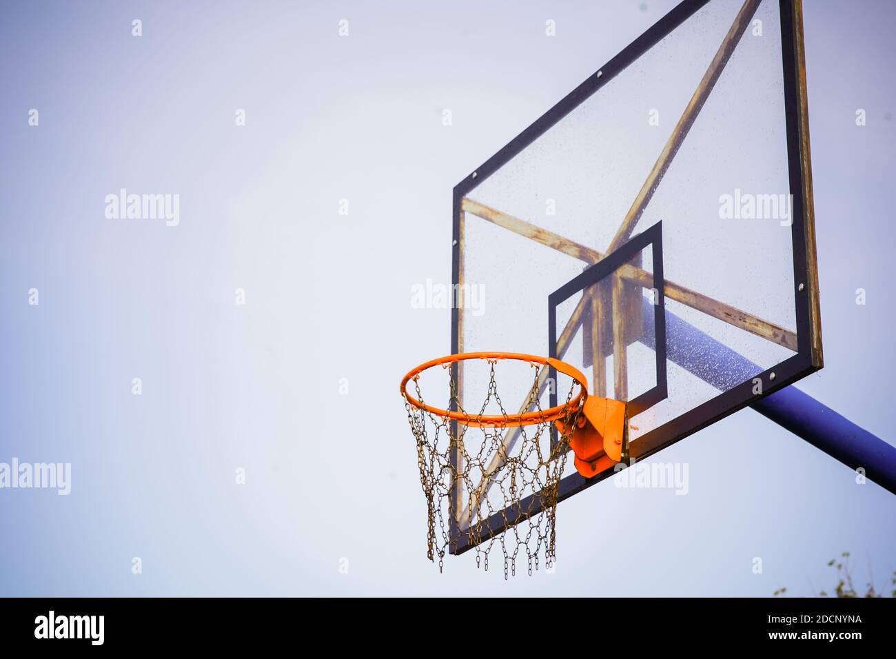 Panier de basket-ball avec plateau transparent et chaînes au lieu de filet contre le ciel bleu clair pendant l'après-midi avec un léger vignetage sombre Banque D'Images