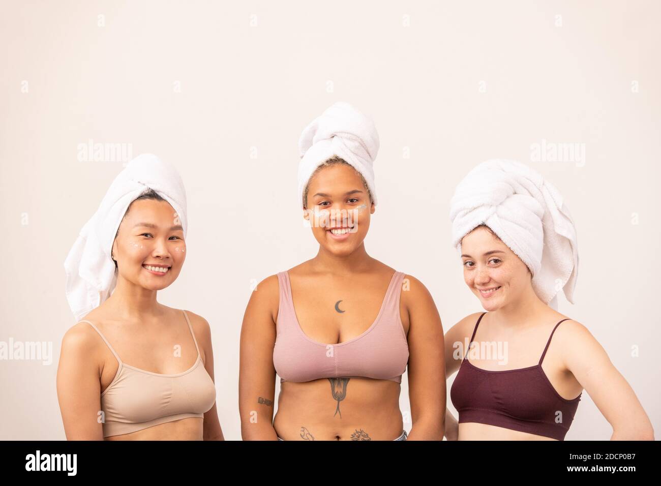 Jolies filles asiatiques, africaines et caucasiennes avec des serviettes douces sur la tête et le bureau Banque D'Images