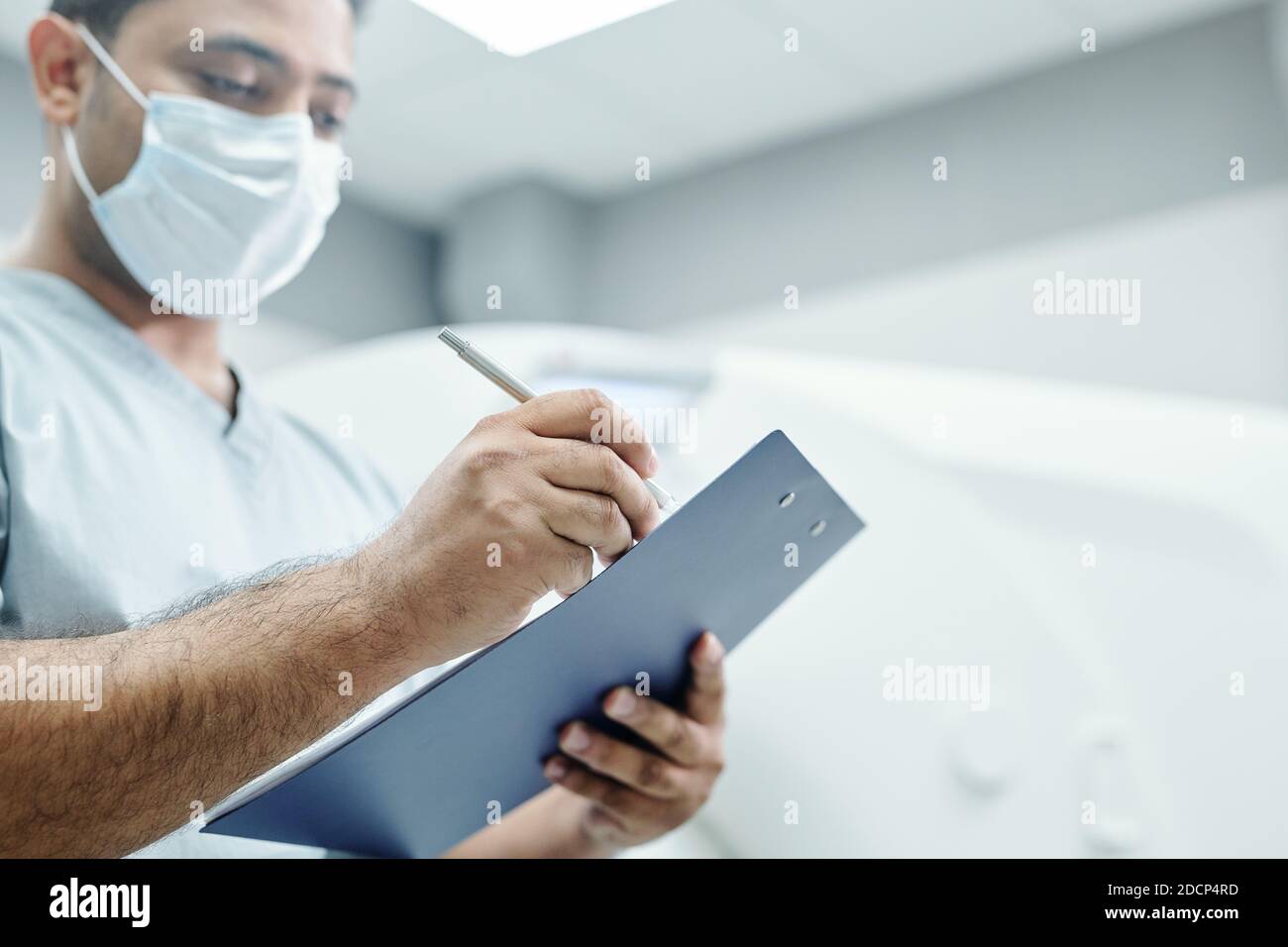 Mains de docteur de race mixte mature en uniforme et masque prendre des notes Banque D'Images