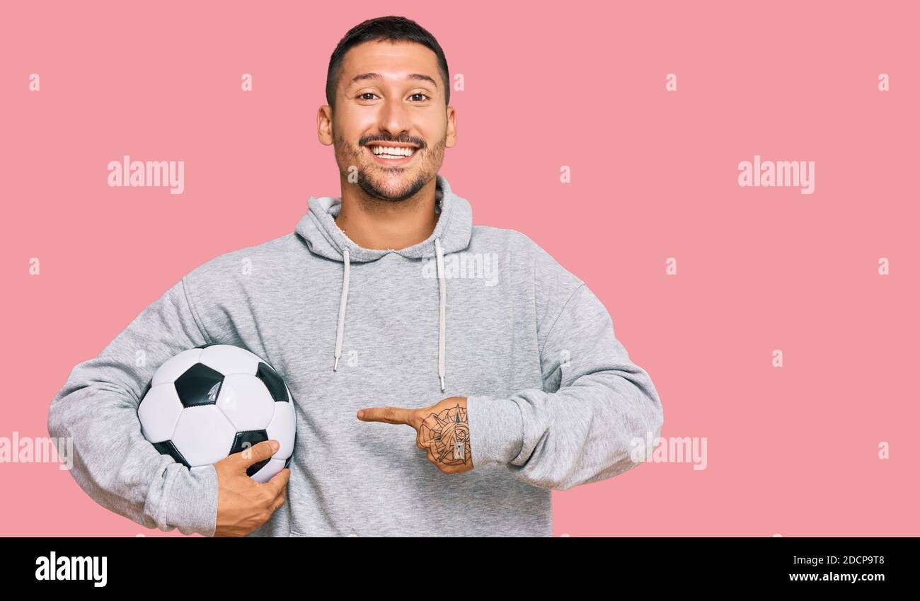 Beau homme avec des tatouages tenant le ballon de football souriant heureux pointage avec la main et le doigt Banque D'Images