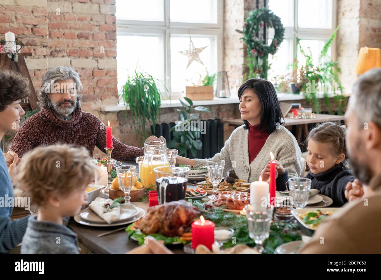 Trois générations de grande famille tenant par les mains tout en priant avant le dîner Banque D'Images