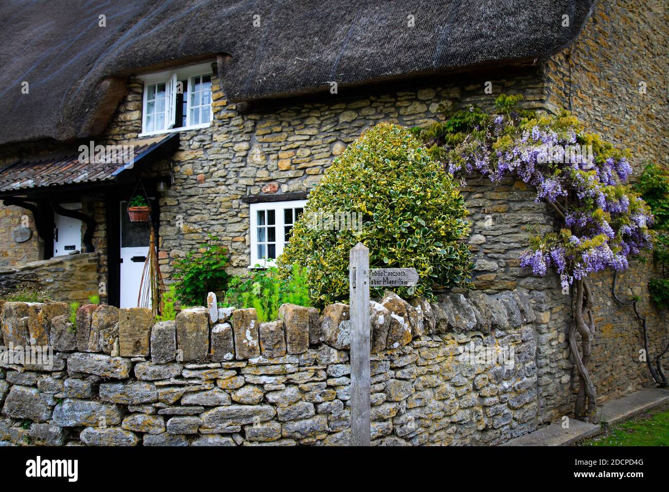 Un cottage au toit de chaume d'importance historique avec panneau de chemin de pied de Coker Moor et wisteria dans East Coker, Somerset, Angleterre Banque D'Images