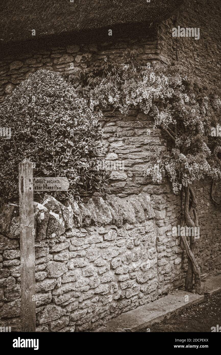 Un cottage en pierre de jambon au toit de chaume d'importance historique avec panneau de chemin de pied de Coker Moor et wisteria à East Coker, Somerset, Angleterre en Sepia Banque D'Images