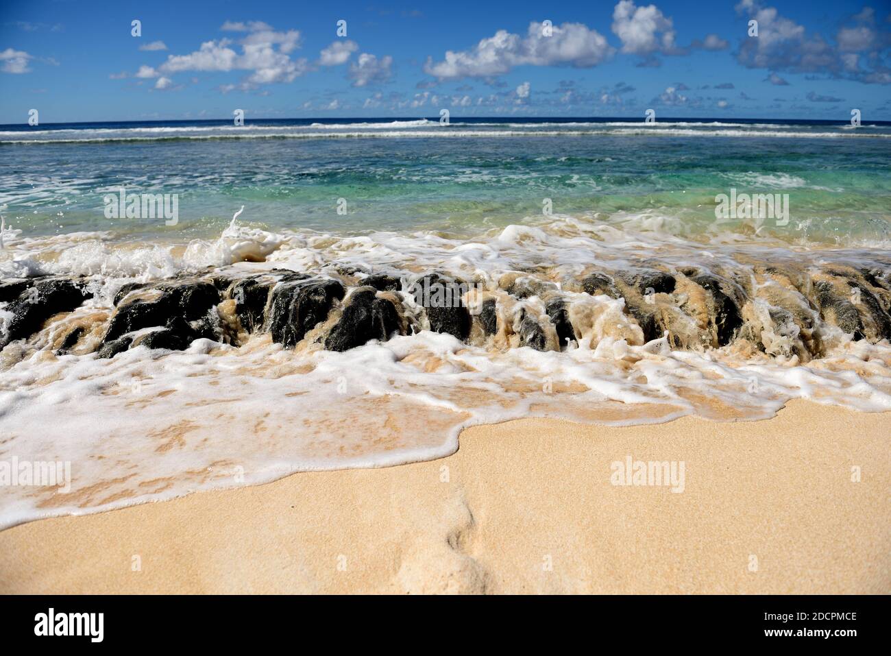 Des vagues de l'océan débordent sur les rochers de récif de lave, la plage de sable, la mer bleue, le ciel et les nuages à Guam, en Micronésie Banque D'Images