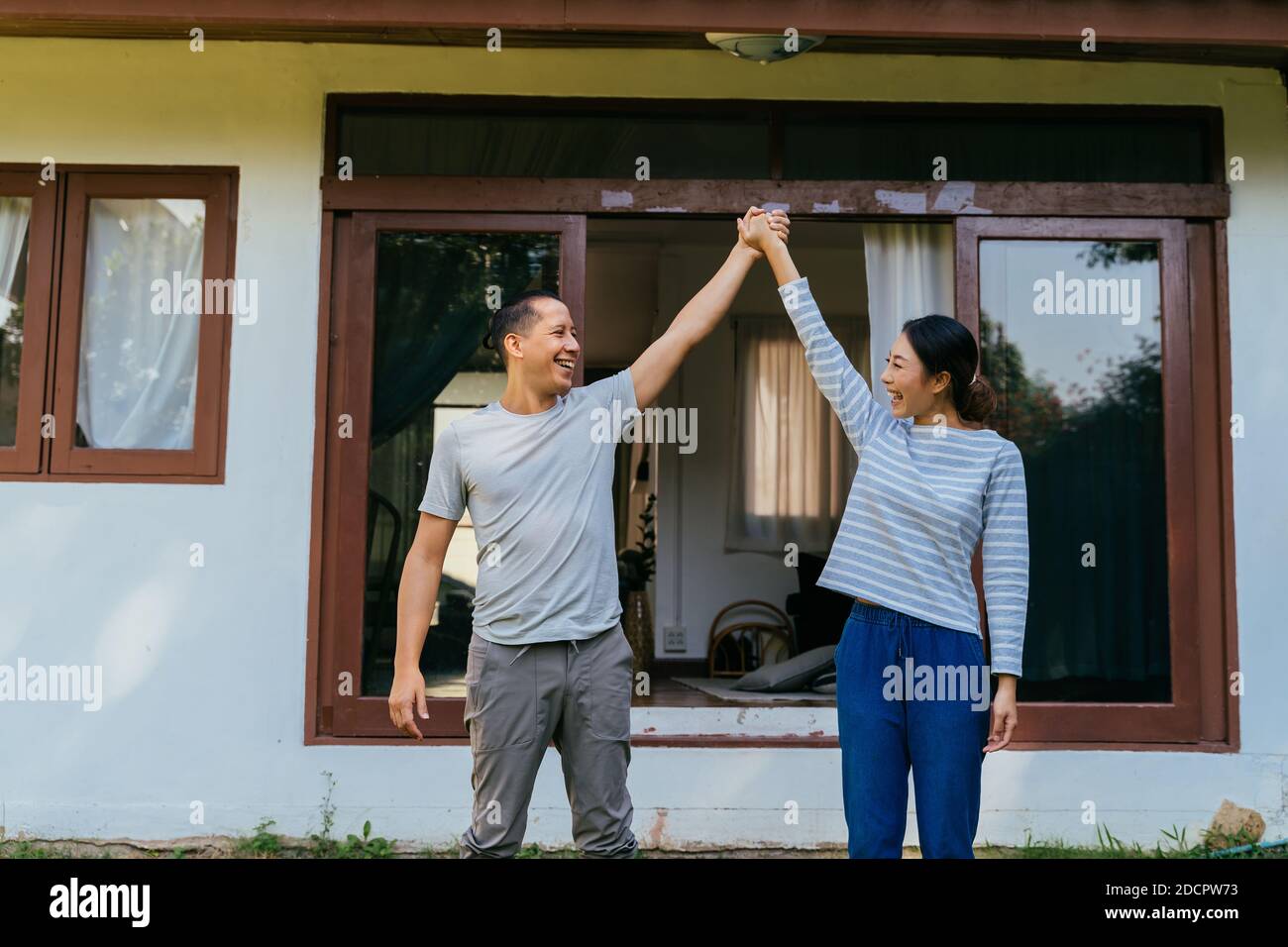Portrait d'un jeune couple asiatique adulte tenant les mains ensemble avec l'intérieur de la maison en arrière-plan. 30s heureux mûr mari et femme souriant. Concept de réalisation immobilière Banque D'Images