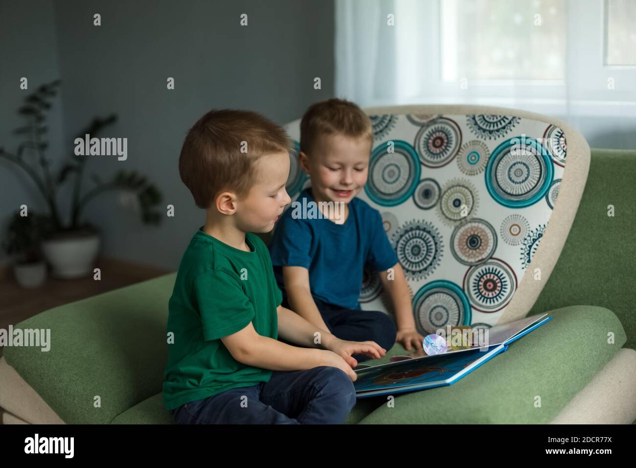 Les enfants à la maison regardent un livre sur le canapé. Banque D'Images