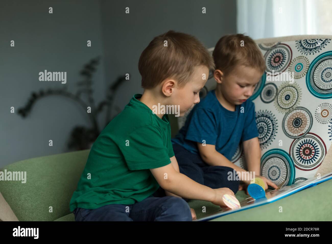 Les enfants à la maison regardent un livre sur le canapé. Banque D'Images