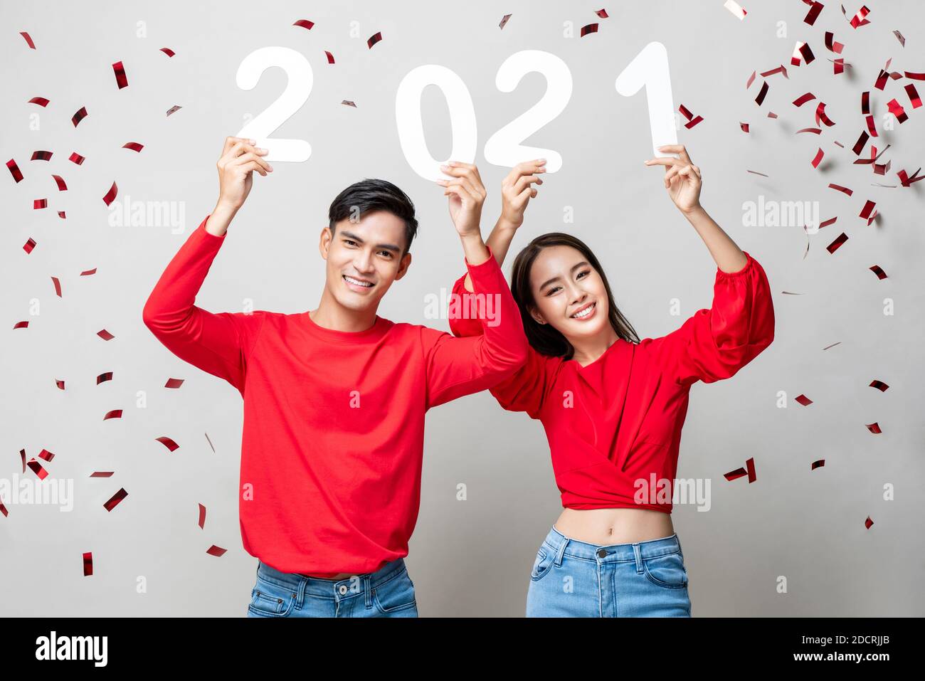 Portrait d'un couple asiatique souriant en tenue décontractée rouge 2021 numéros pour le nouveau concept de l'année en gris clair arrière-plan avec confetti Banque D'Images